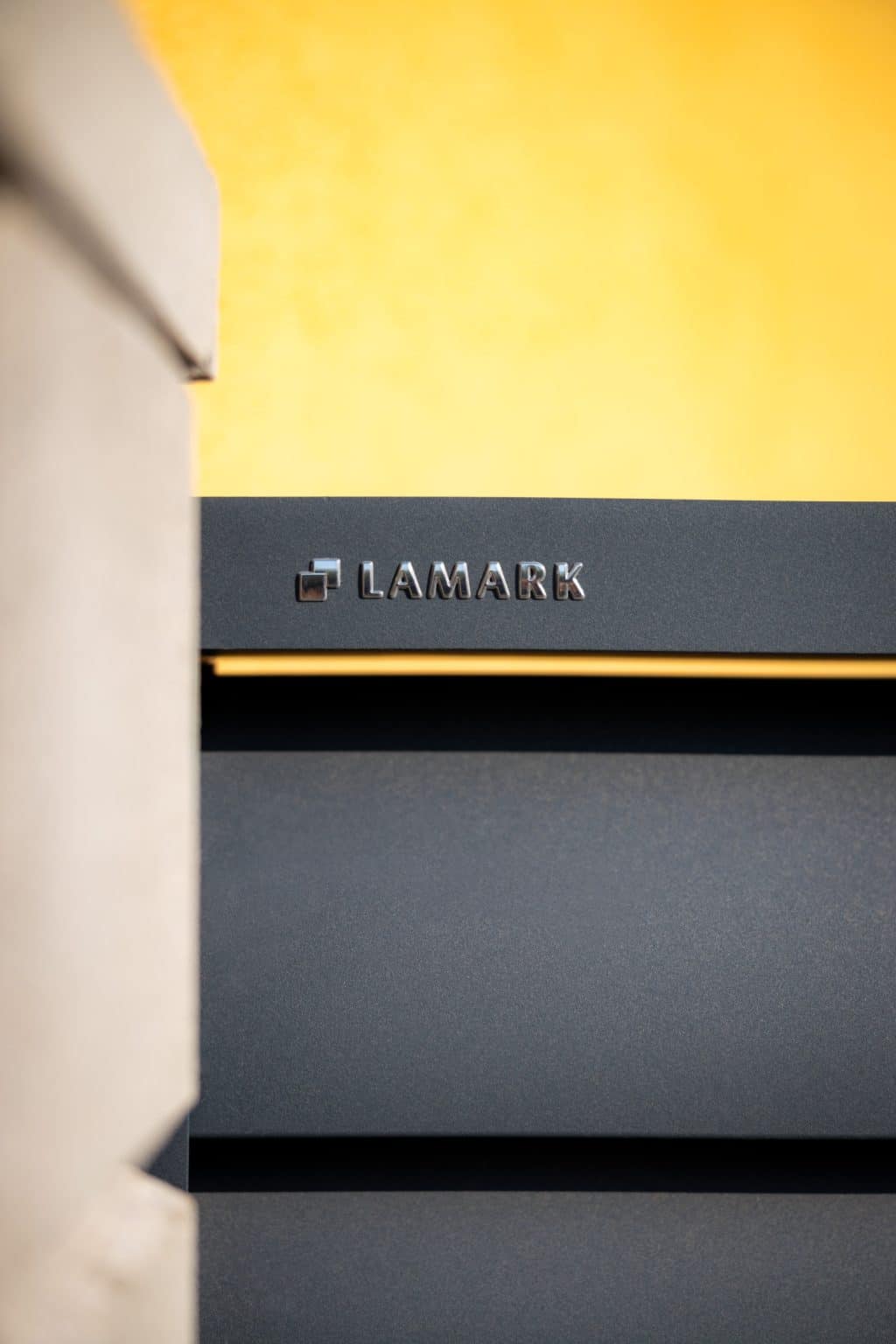 Detail loga LAMARK na hliníkové samonosné posuvné bráně | Motiv Pamplona | Šedá antracitová barva | Zděné sloupky