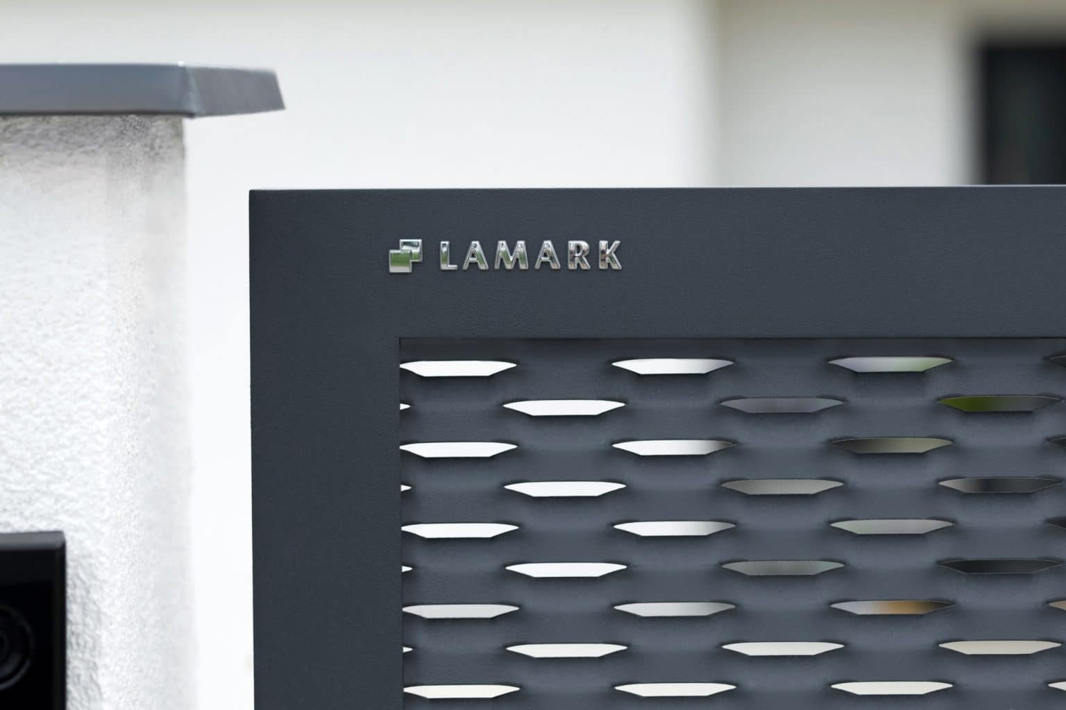 Detail loga LAMARK na jednokřídlé brance LAMARK z tahokovu | Motiv Madeira | Šedá antracitová barva | Zděné sloupky | Nechanice