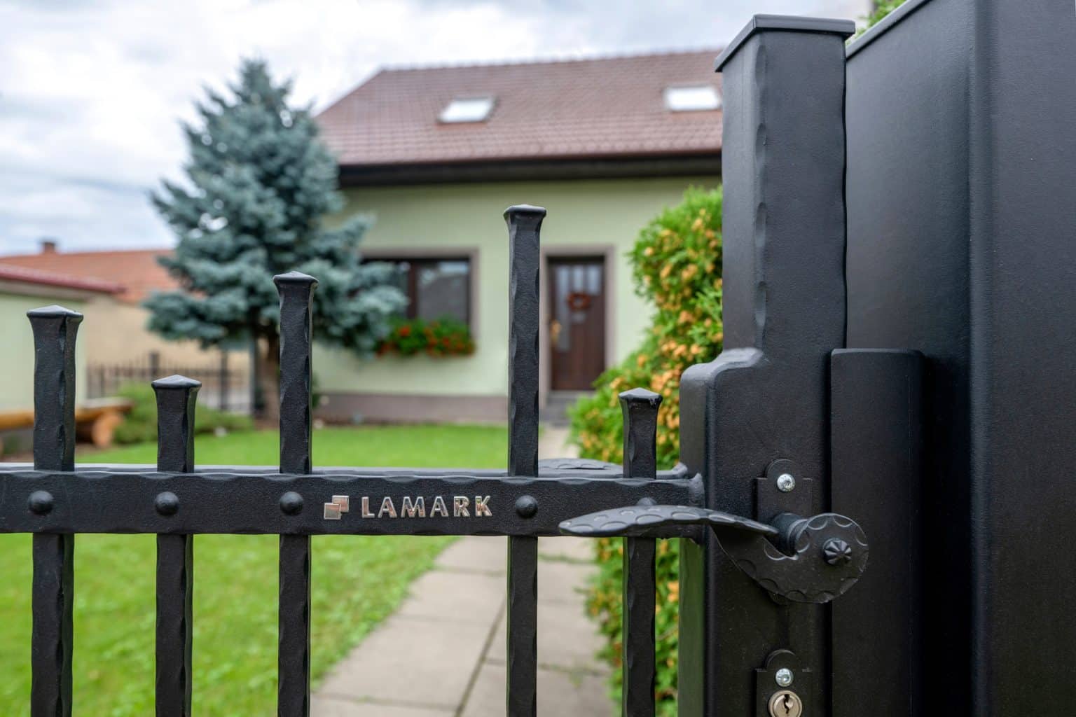 Detail kliky a loga na kované brance LAMARK | Motiv Singapur | Černá kovářská barva | Svařované s nýty | Oklepávané provedení | Okované konce | Hliníkové sloupky LAMARK