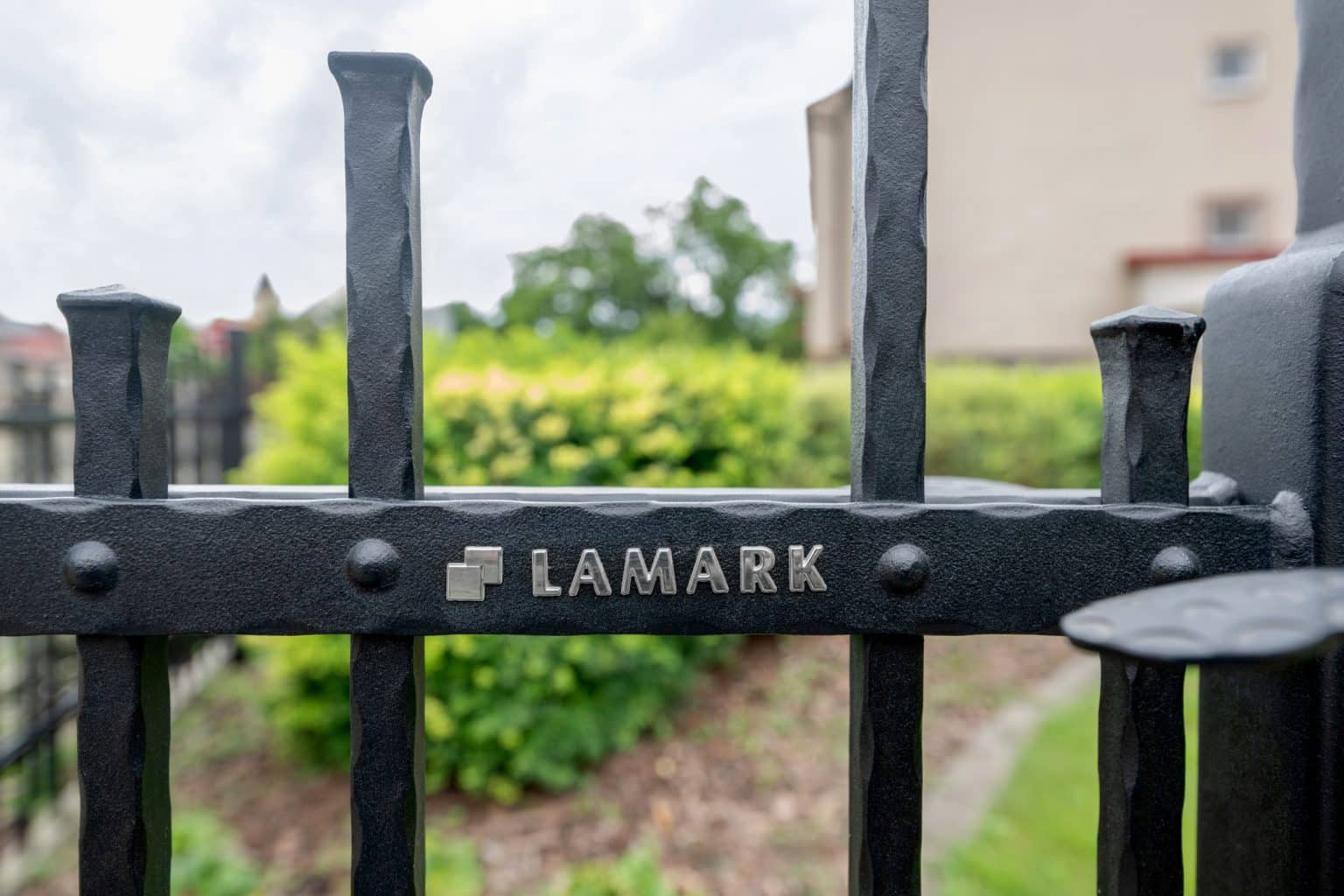 Detail loga LAMARK na kované brance | Motiv Singapur | Černá kovářská barva | Svařované s nýty | Oklepávané provedení | Okované konce | Hliníkové sloupky LAMARK
