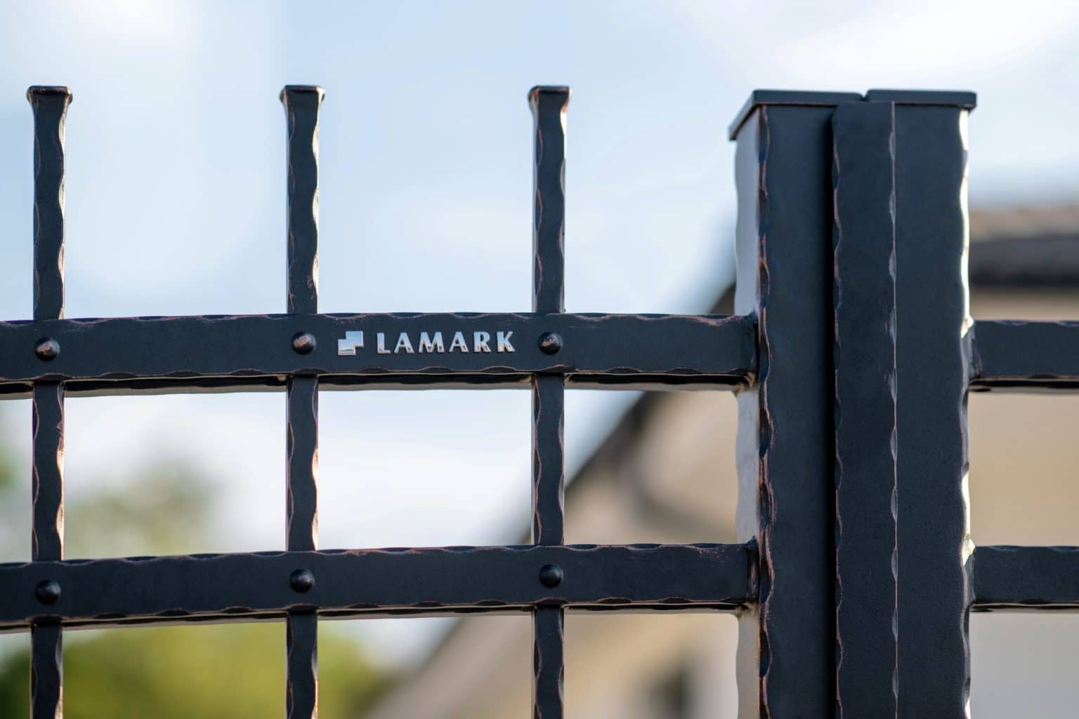 Detail loga LAMARK na kované bráně | Motiv Havana | Černá kovářská barva | Měděná patina | Svařované s nýty | Oklepávané provedení | Okované konce | Zděné sloupky