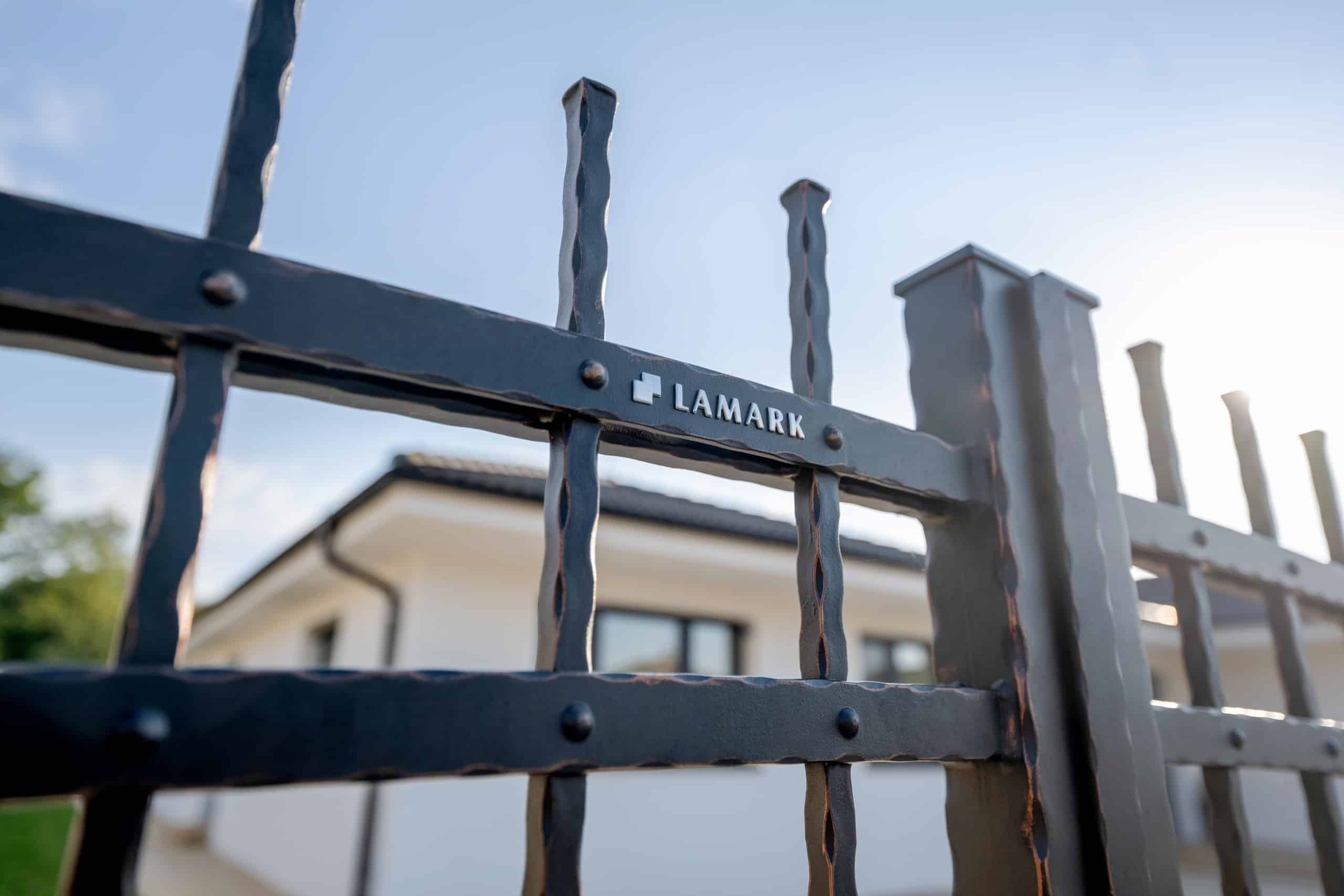 Detail loga LAMARK na kované bráně | Motiv Havana | Černá kovářská barva | Měděná patina | Svařované s nýty | Oklepávané provedení | Okované konce | Zděné sloupky